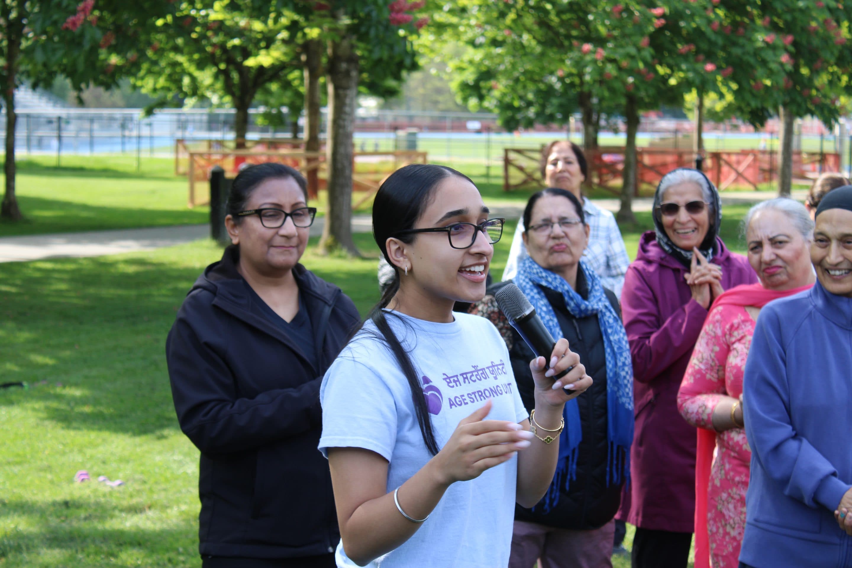 A young volunteer addressing the gathering, with older women smiling in the background.