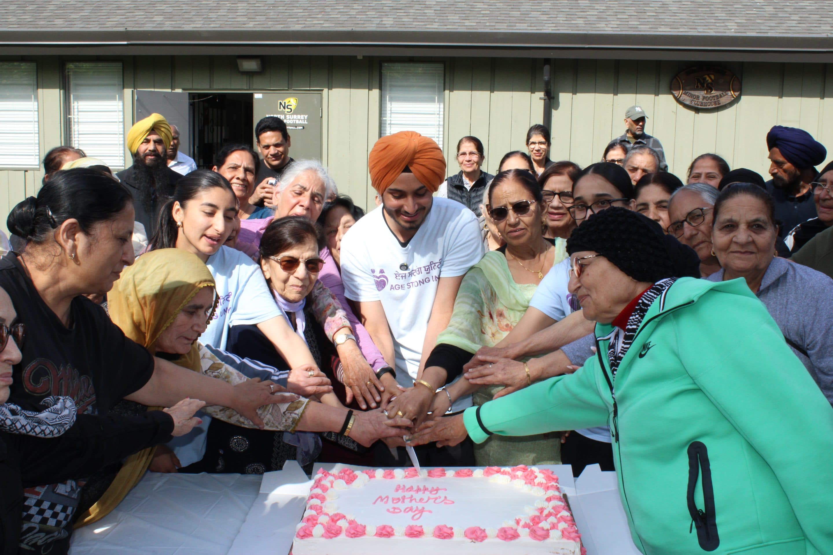 Many hands together on a single knife, cutting a Mother's Day cake.