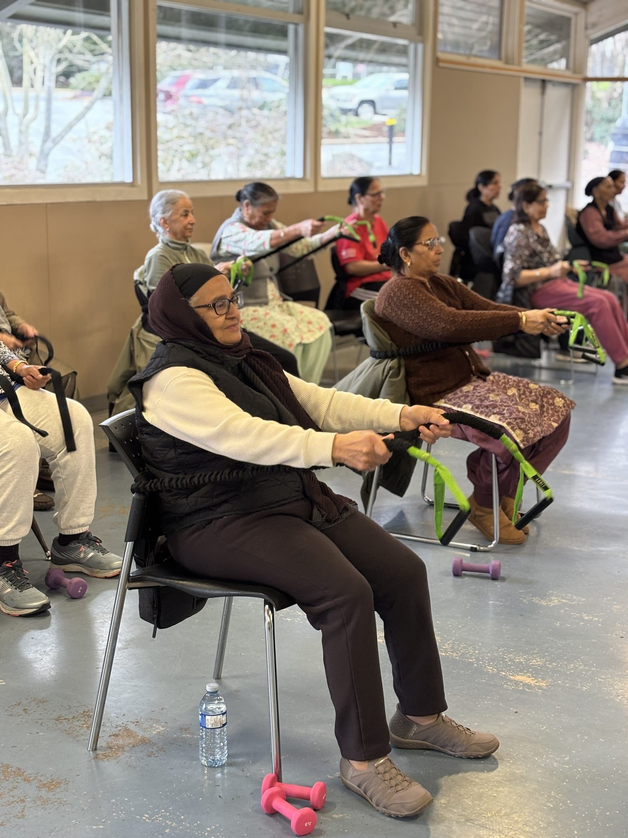 An older woman seated and pulling on a green resistance band during class.