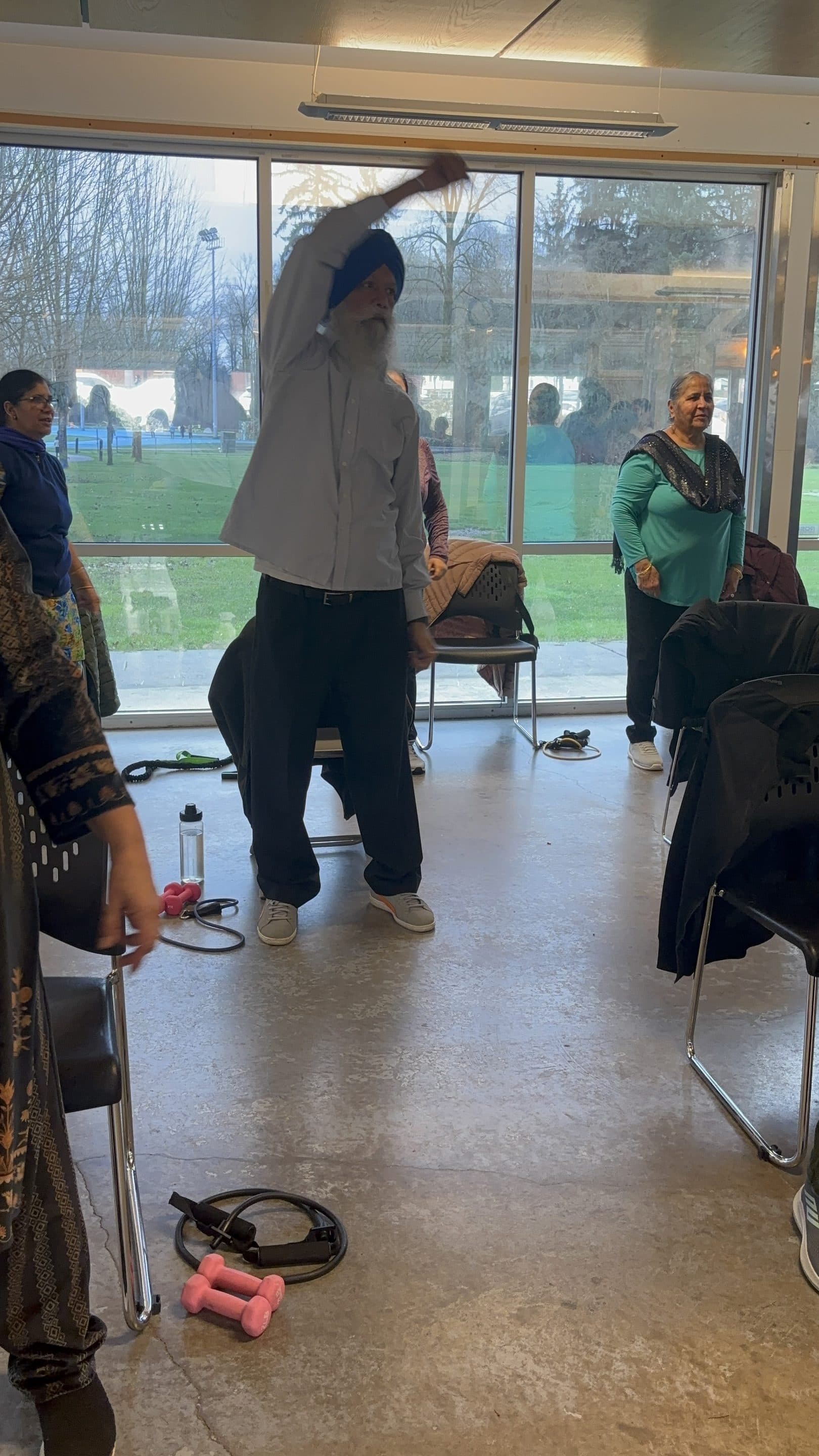 A community member doing a standing side-stretch in class, with classmates visible behind.